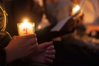 Menschen halten im dunkeln Osterkerzen und Liedblätter
